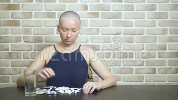 一个年轻的秃头女人坐在一张靠在砖墙上的桌子旁悲伤地看着药丸复制空间视频的预览图
