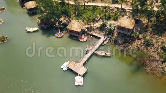 平房与茅草屋顶和船墩在岸上绿湖鸟瞰热带湖岸上的避暑别墅视频的预览图