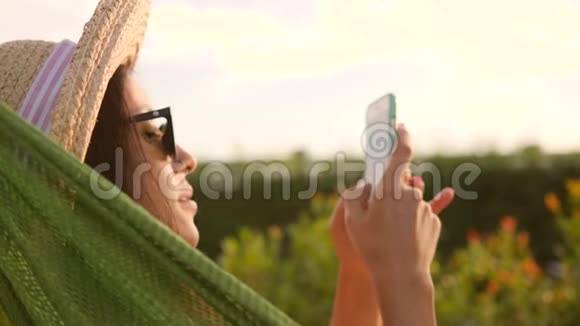 夕阳下公园吊床上一位迷人的女游客在看手机泰国普吉岛4K慢行视频的预览图