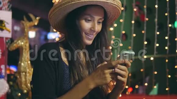 年轻混合种族少女短信问候信息智能手机与圣诞树背景4K视频的预览图
