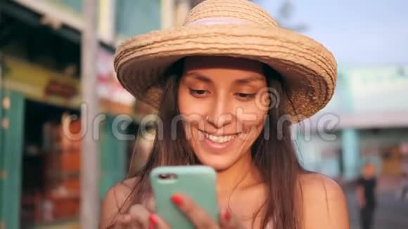 年轻的无忧无虑的快乐嬉皮士女人在老旧建筑使用移动电话的草帽混合种族旅游女孩视频的预览图