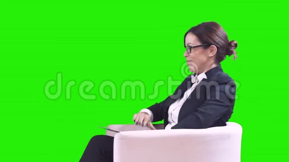 电视演播室戴眼镜的深色头发她穿着西装坐在工作室里接受采访绿色视频的预览图
