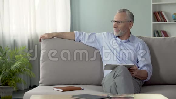 成年男性坐在沙发上在平板电脑上预订度假酒店房间视频的预览图