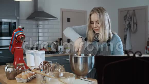 年轻漂亮的女人把配料混合在碗里准备面团烘焙厨房里的金发女郎视频的预览图