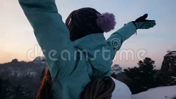 一位年轻的女登山者站在山顶上看日落视频的预览图