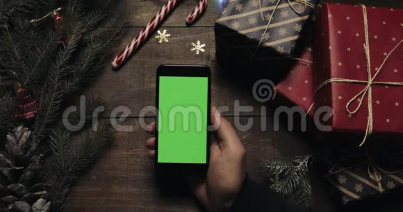 男性手拿着绿色屏幕的黑色智能手机另一只手把一些礼物盒放在桌子上铬键视频的预览图