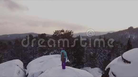 一位年轻的女登山者站在山顶上看日落视频的预览图