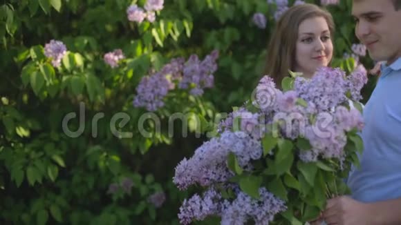 在夕阳下的夏日花园里带着一束紫丁香的可爱男女视频的预览图