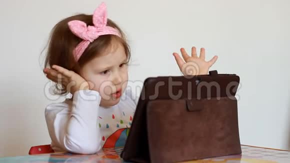 孩子看平板电脑屏幕播放下载的应用程序一个小可爱的女孩坐在桌子旁看电视视频的预览图
