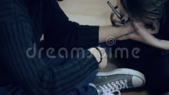女人用钢笔在坐在室内地板上的男人的手腕上画画视频的预览图