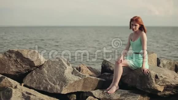 美丽的女孩坐在海边的岩石上视频的预览图
