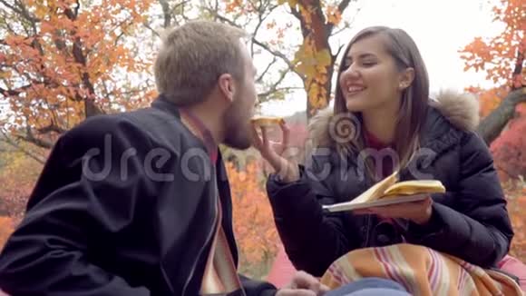 一个快乐的女人正在秋天公园的中央给一个长胡子的男人喂一个夹心奶酪慢动作视频的预览图
