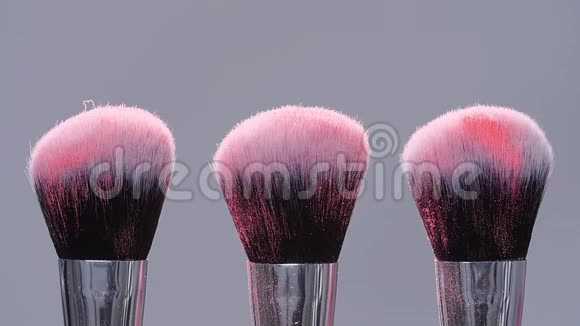 化妆刷与粉红色粉末溅在灰色背景爆炸慢动作视频的预览图