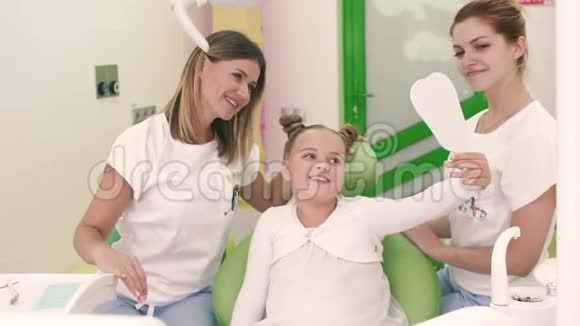 穿着白色连衣裙的小女孩和两位牙医微笑着向相机竖起大拇指视频的预览图