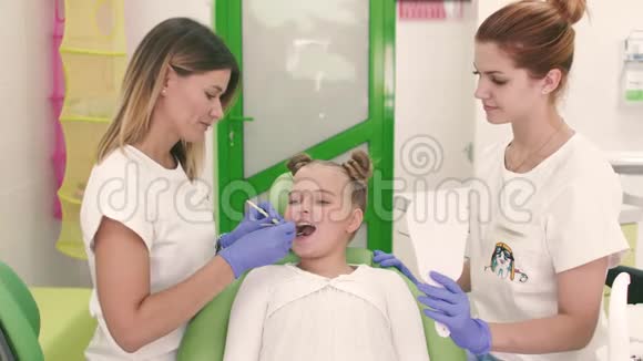 儿童和家庭牙医妇女在你的嘴里看牙齿有一个美丽的小女孩坐在旁边视频的预览图