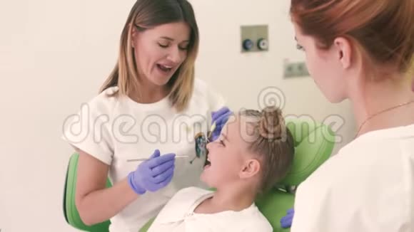 坐在牙科椅上的小女孩牙医和她的助手在看牙齿他们彼此微笑视频的预览图
