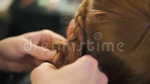 她是一个理发师的手她正在为一个漂亮的头发模特编织辫子把头发合上视频的预览图