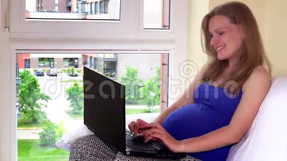 怀着幸福的未来妈妈带着笔记本电脑女性在家玩得开心视频的预览图