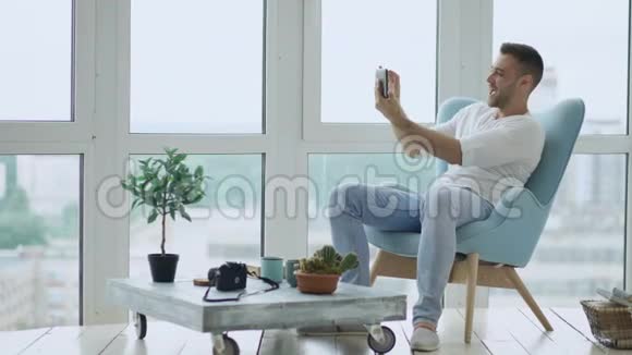 年轻的快乐男人在现代阁楼办公室里坐在阳台上用数码平板电脑进行在线视频会议视频的预览图