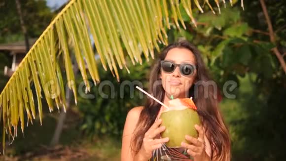年轻的快乐混合种族妇女在热带海滩喝新鲜的泰国椰子水鸡尾酒4K泰国普吉岛视频的预览图