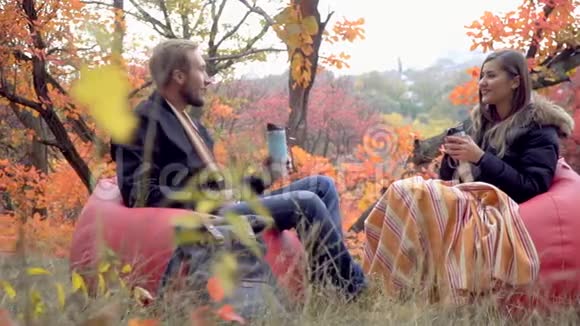 在秋天的森林里一对情侣坐在泡芙上他们用热水瓶喝酒交流慢动作视频的预览图