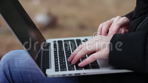 在秋日公园的长椅上女性手在笔记本电脑上打字视频的预览图