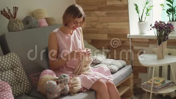 微笑的女人坐在家庭作坊的沙发上编织羊毛衫视频的预览图