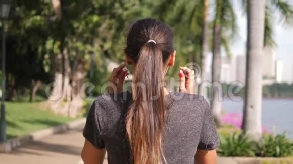 年轻的混合种族健身女孩戴上耳机并开始运行健身在城市公园4K慢动作视频的预览图
