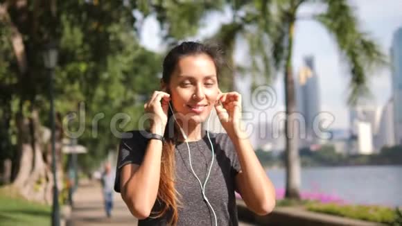 年轻的混合种族健身跑步者女士在城市公园和大办公室安装和使用移动智能手表耳机视频的预览图