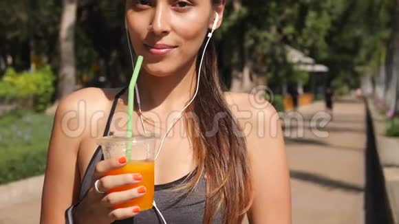 城市公园微笑快乐跑者女孩在健身后喝新鲜橙汁的肖像4K慢动作泰国视频的预览图