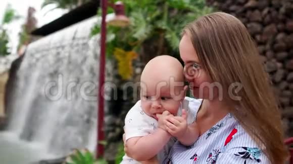母亲带着孩子微笑拥抱婴儿的儿子关于瀑布亲吻和与他交谈幸福的概念视频的预览图