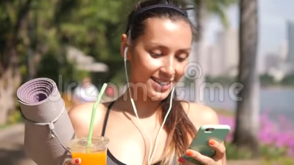 城市公园晨练瑜伽后年轻混合种族运动员使用智能手机和饮用新鲜橙汁视频的预览图
