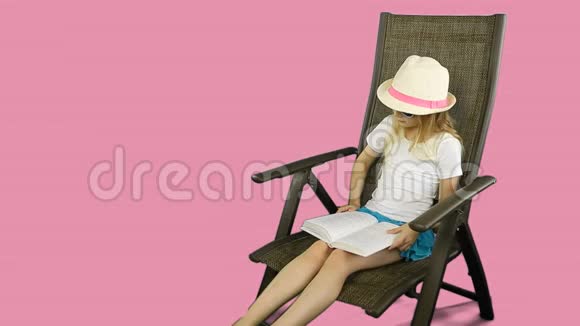 年轻的白种人女孩穿着白色的t恤和帽子坐在椅子上仔细阅读书籍视频的预览图