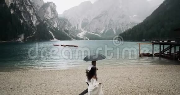 奇妙的风景大湖大山下雨天一对夫妇在伞下奔跑走向木头视频的预览图