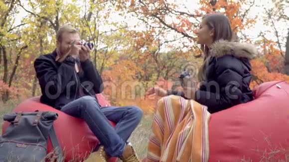 爱情故事一个男人拿着相机拍他的女朋友的照片女朋友坐在有热水瓶的软垫凳子上然后视频的预览图