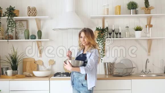 金发女人在厨房的炉子旁的桌子上用碗搅拌视频的预览图