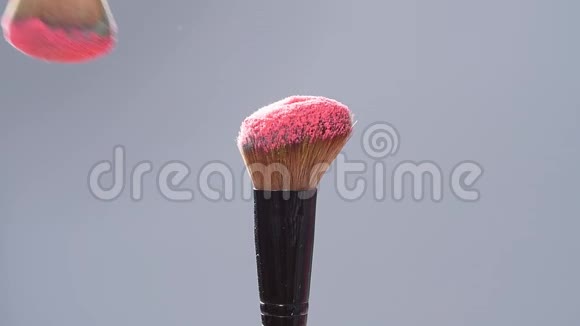 化妆刷与粉红色粉末溅在灰色背景爆炸慢动作视频的预览图