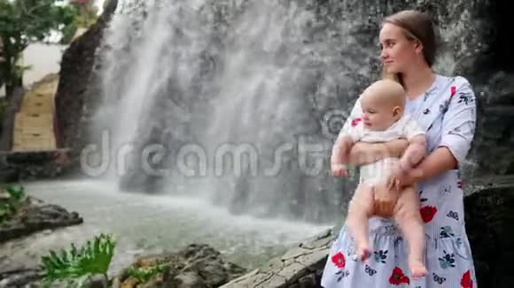 母亲带着孩子微笑拥抱婴儿的儿子关于瀑布亲吻和与他交谈幸福的概念视频的预览图