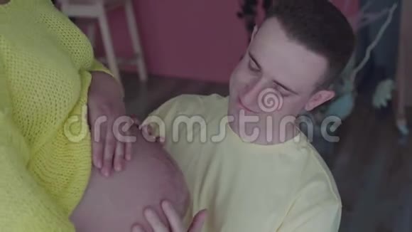 幸福的夫妻在家丈夫拥抱和抚摸怀孕的妻子的肚子慢动作视频的预览图