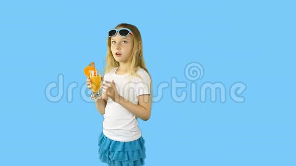 穿着白色t恤的年轻女孩调情从玻璃杯里喝橙汁快乐女孩用吸管喝橙色鸡尾酒视频的预览图