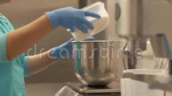 女面包师把面粉倒入碗里站在餐厅的厨房秤上视频的预览图