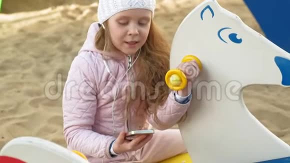 小女孩骑着秋千用耳机打电话视频的预览图