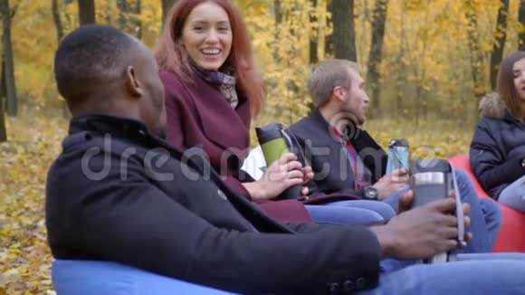 有热水瓶的朋友坐在秋天公园的沙发上聊天有点慢动作视频的预览图