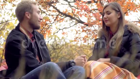 可爱的一对夫妇坐在秋天的公园里坐在垫着的凳子上手牵着手看着对方的眼睛慢动作视频的预览图