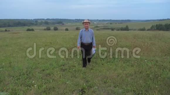 帽子里的一个老农夫拿着电话和文件夹走在田野上视频的预览图