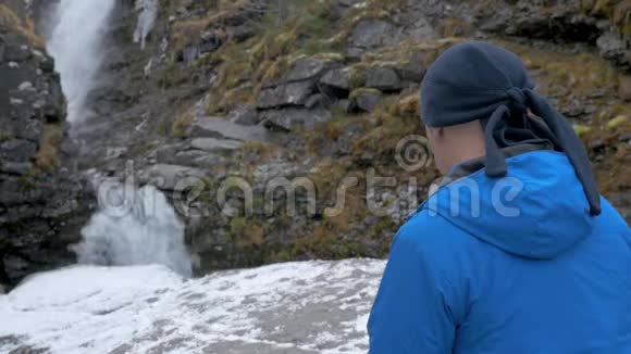 一个穿着运动服的人在瀑布前休息他在智能手机上拍摄风景视频的预览图