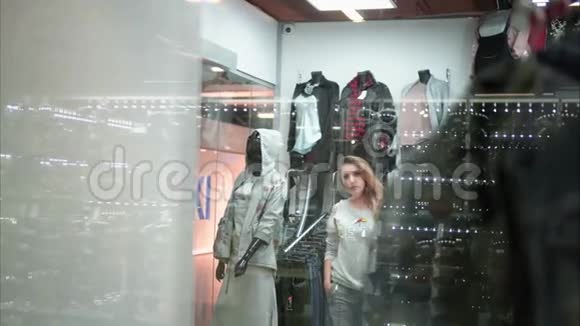 女孩在商店里试穿一件新的时尚毛衣通过窗口查看购物视频的预览图