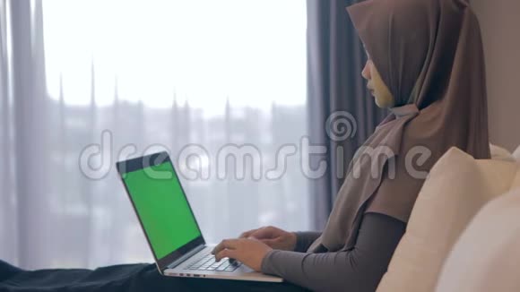 年轻的亚洲穆斯林妇女使用带绿色屏幕的笔记本电脑视频的预览图