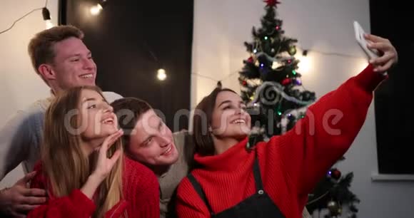 新年庆典两对年轻夫妇坐在圣诞树前的智能手机上自拍视频的预览图
