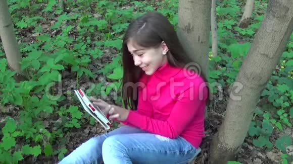 美丽的少年女孩带着平板电脑坐在公园的草地上微笑可爱的女学生录像镜头拍摄视频的预览图
